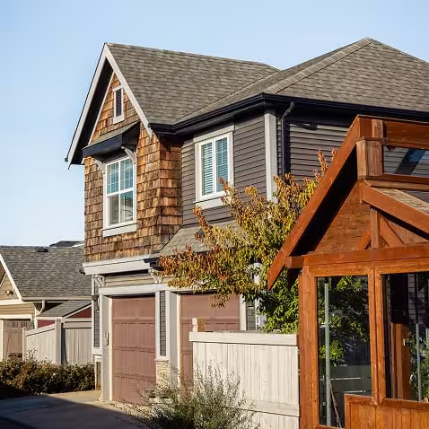 Rear view of a Griesbach home with garage doors, wood accents, fencing, and a backyard deck.
